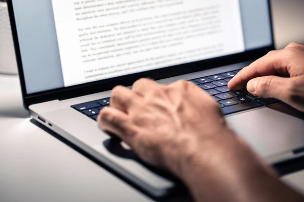 Rrmote content writer working Close-up of hands typing on a laptop keyboard with blurred screen text.